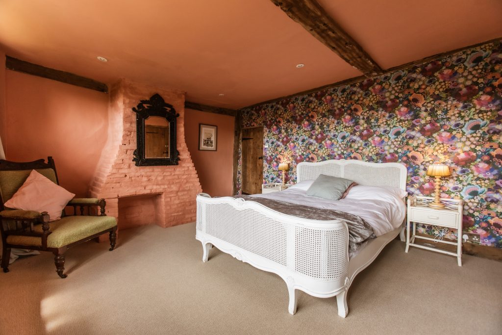 Whitfield House flower room with floral wallpaper and pink walls with a large king bed in white rattan.
