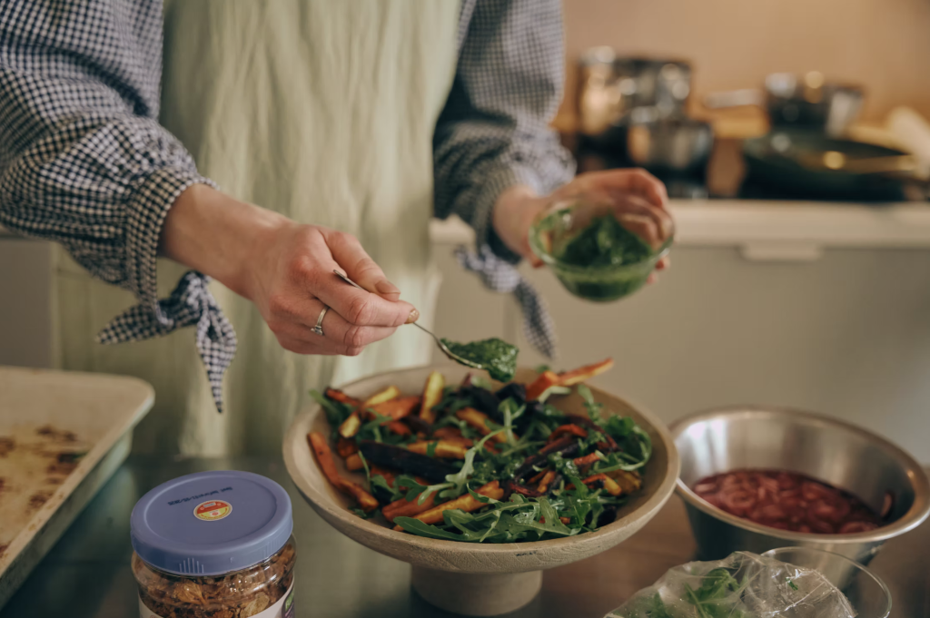 Laura Paint chef drizzling green sauce onto a large salad.
