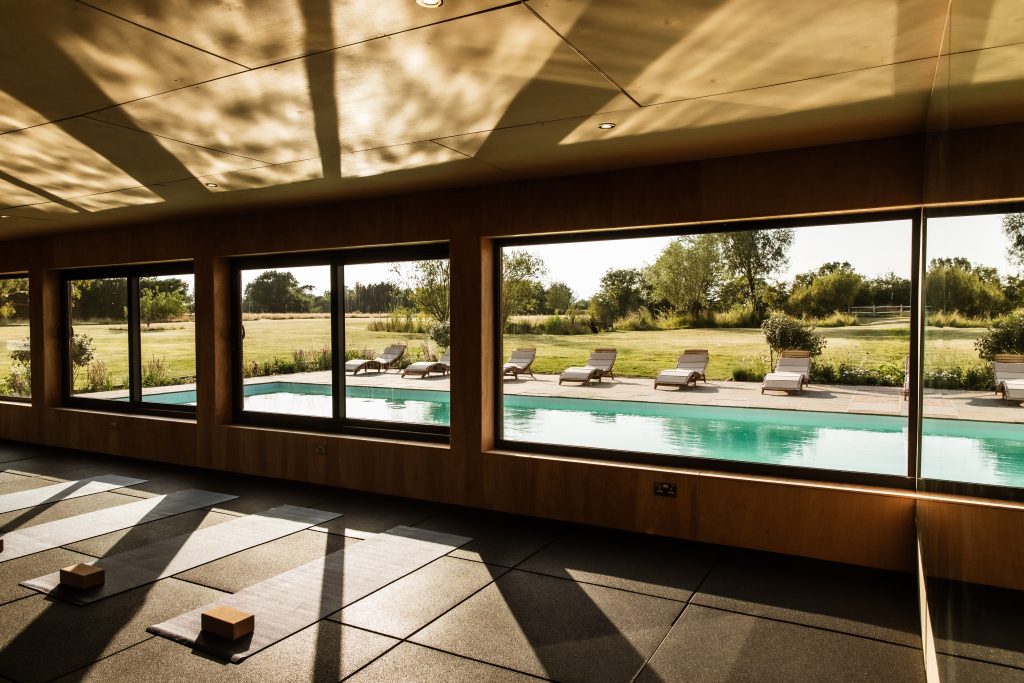 Whitfield House Yoga room with view over the pool. Sunlight streaming through the windows and yoga mat and bricks set out on the floor. Viewed at an angle inside.