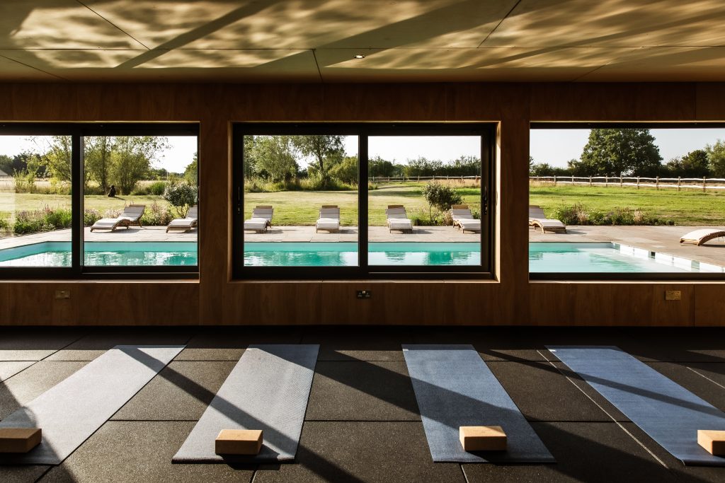 Whitfield House Yoga room with view over the pool. Sunlight streaming through the windows and yoga mat and bricks set out on the floor. Viewed straight on inside.
