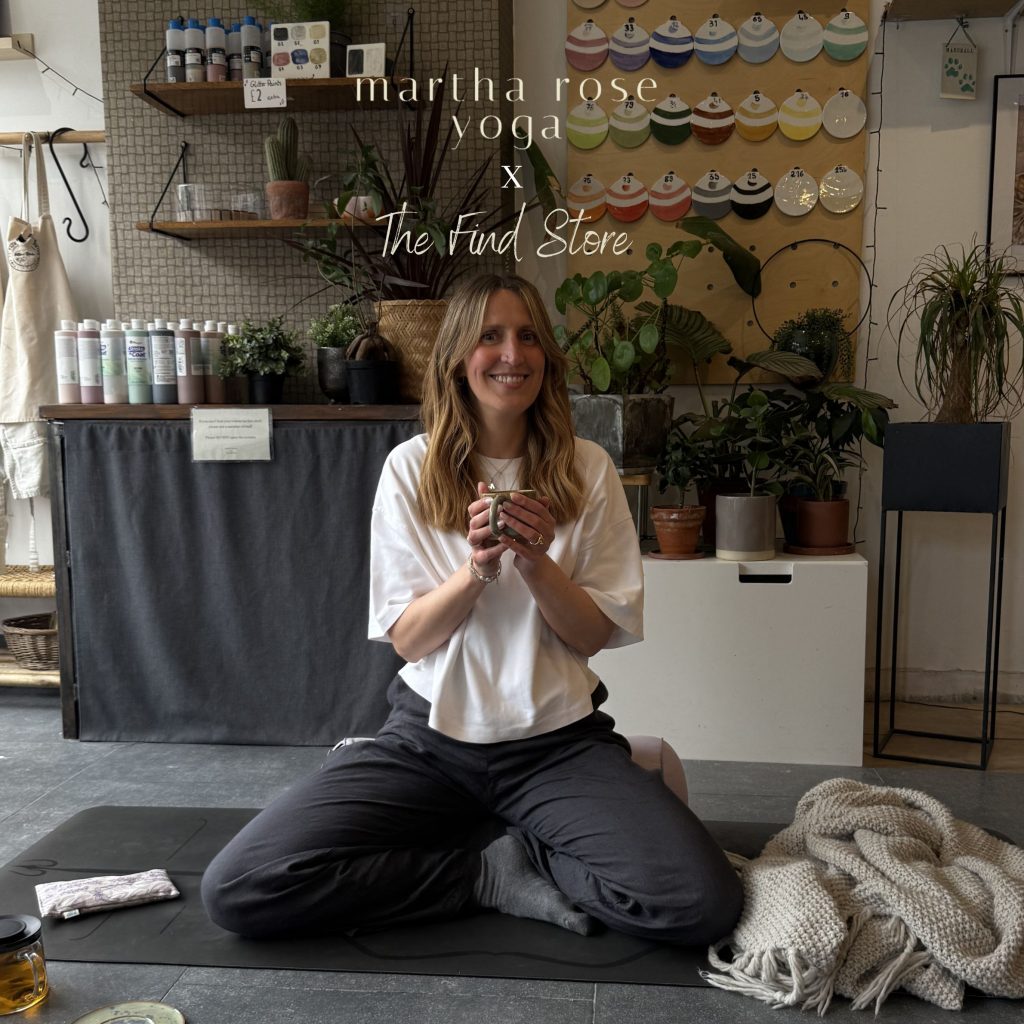 Martha chapman sitting on a bolster drinking tea in The Find Store, surrounded by pottery, paining, plants, blanket and more