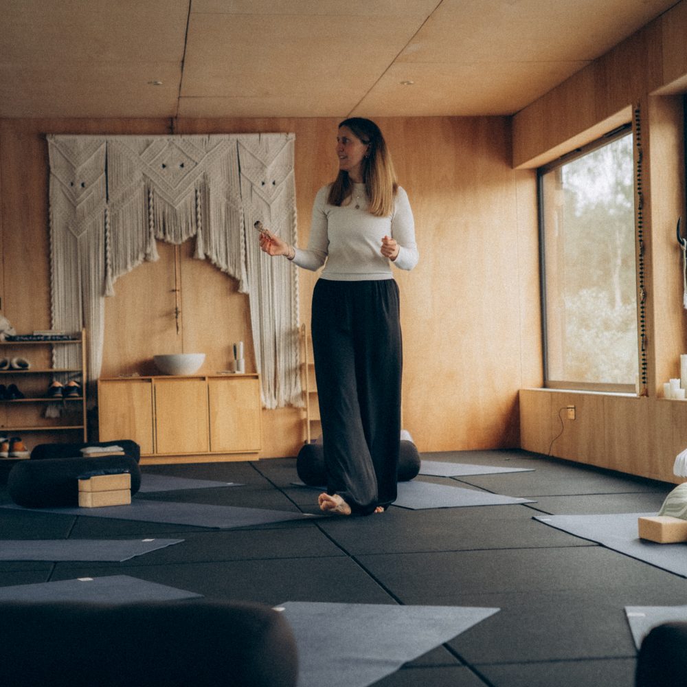 Martha setting up yoga studio with bolsters, mats, bricks at Biddenden House. Large windows in the background. Martha burning sage